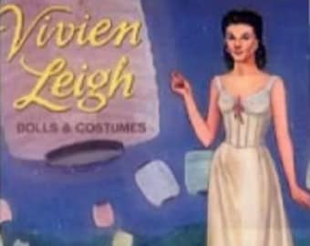 Op de afbeelding: Een vintage papieren poppenset met Vivien Leigh, een beroemde actrice. De set bevat poppen en kostuums. De afbeelding toont een pop gekleed in een witte jurk met een kantversiering. De achtergrond toont een blauwe lucht met witte wolken.