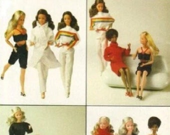 May include: A collection of dolls wearing a variety of outfits. The dolls are all dressed in different colours and styles of clothing. Some of the dolls are wearing dresses, while others are wearing trousers and shirts. The dolls are all standing on a white background.