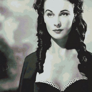 May include: A black and white portrait of a woman with dark hair styled in loose curls. She is wearing a low-cut black dress with a white lace trim.