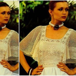 May include: A white crochet top with a square neckline and a geometric pattern. The top has a wide, flowing cape-like sleeve. The model is wearing a beaded necklace.