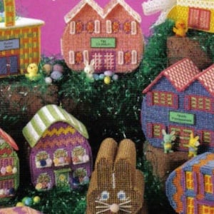 May include: A collection of colorful, hand-stitched Easter-themed houses and a bunny rabbit. The houses are decorated with stripes, polka dots, and flowers. The bunny is brown with white eyes and whiskers.