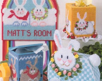 May include: Three plastic canvas tissue box covers featuring bunny rabbits. The first cover is a blue and white design with two bunnies holding a sign that says "Matt's Room". The second cover is yellow with a bunny wearing a flower crown. The third cover is blue and white with a bunny wearing a flower crown.