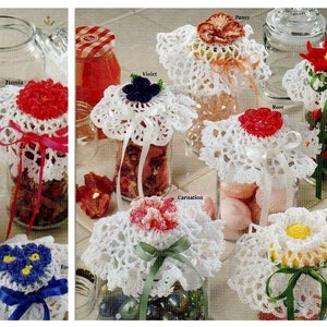 Könnte beinhalten: Neun Glasgefäße mit gehäkelten Deckeln, die mit verschiedenen Blumen verziert sind. Die Gläser sind mit verschiedenen Gegenständen gefüllt, wie zum Beispiel getrockneten Blumen, Süßigkeiten und anderen kleinen Gegenständen. Die Deckel sind mit den Namen der Blumen beschriftet, wie zum Beispiel "Zinnia", "Veilchen", "Nelke", "Gänseblümchen", "Rose", "Weihnachtsstern", "Stiefmütterchen" und "Gänseblümchen".