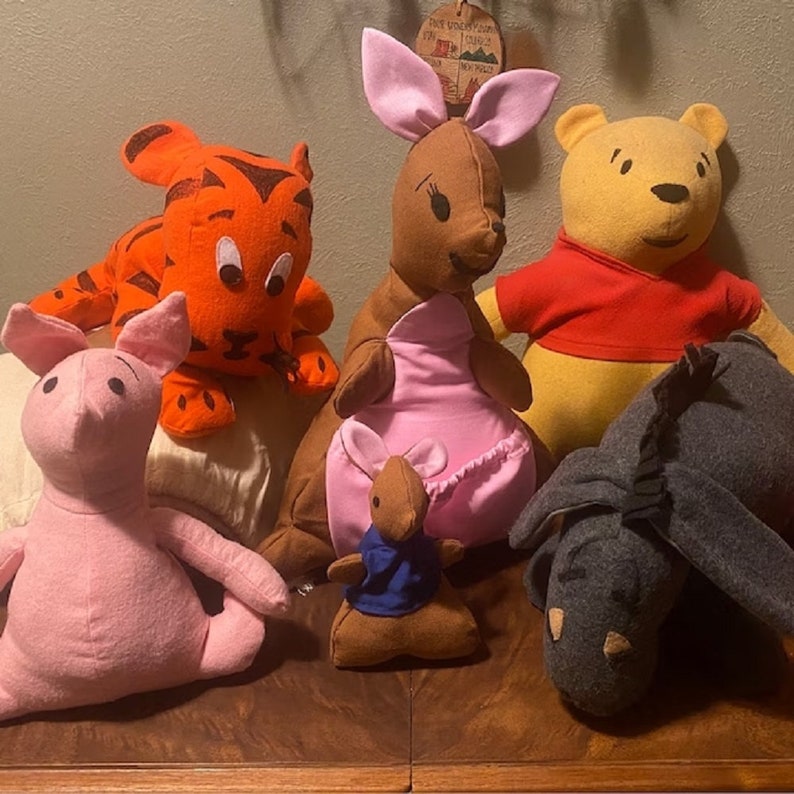 May include: A group of handmade plush toys depicting characters from a well-known children's story. The toys include a tiger, a kangaroo with a joey, a bear, a pig, and a donkey. Each toy is made of soft fabric in various colours.