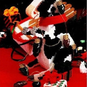 May include: A black and white cow figurine holding a red and white gift box with a bow. The cow is surrounded by Christmas lights and a red background.