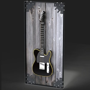 Puede incluir: Una guitarra eléctrica negra con ribete amarillo está montada sobre un panel de madera envejecida. El panel está enmarcado con escuadras de metal negro. El mástil y la pala de la guitarra son visibles, mostrando las clavijas y los trastes.