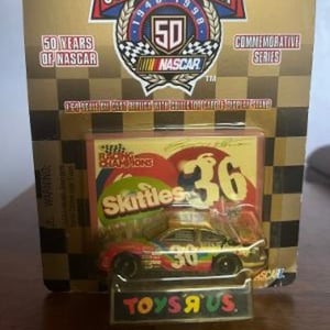 May include: A NASCAR Racing Champions die-cast car, featuring a Skittles paint scheme, with the number 36. The car is displayed in its original packaging, with the Toys R Us logo visible. The packaging commemorates 50 years of NASCAR.