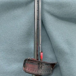 May include: A silver torque wrench with a black handle. The wrench has a gauge with numbers and a red indicator. The handle is textured and the wrench is on a light blue background.