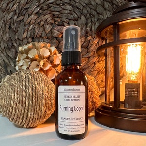 May include: A brown glass bottle with a black spray nozzle and a white label. The label reads "Moonstone Essences Stress Relief Collection Burning Copal Fragrance Spray Hand-Crafted in Columbus, Ohio Phthalate-Free | Organic | Non-Toxic Net. Wt. 2 Oz (59 ml)"