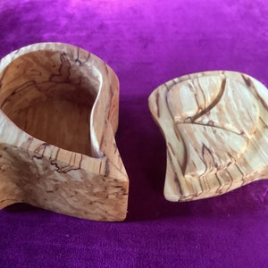 Peut inclure: Une boîte en bois de forme abstraite unique. La boîte est en bois clair avec des stries brunes et brun rougeâtre. La boîte est ouverte, révélant l'intérieur de la boîte.