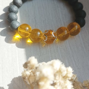 Peut inclure: Bracelet de perles composé de perles gris foncé, gris clair et ambrées, avec une perle décorative argentée. Le bracelet est présenté sur une surface claire, avec des fleurs séchées. Les perles mesurent environ 1 cm de diamètre.