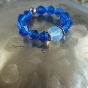 Peut inclure: Une bague de perles bleues avec des perles de cristal facettées et une perle ronde bleu clair. La bague est posée sur une surface métallique. Il s'agit d'un bijou.