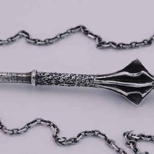 May include: A silver-toned metal pendant shaped like a medieval mace with a textured handle and a flanged head, suspended from a matching silver-toned link chain. The metal features a dark, oxidized finish that highlights the intricate details.