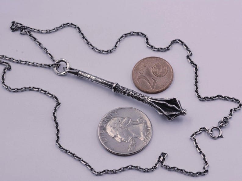 May include: A silver-toned metal mace pendant on a matching link chain, displayed alongside a U.S. quarter coin for scale. The pendant features a textured handle and a multi-flanged head, showcasing a detailed, weathered metallic finish throughout.