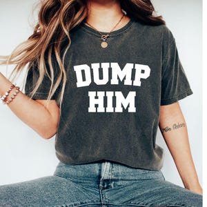 May include: A dark gray t-shirt with the text "DUMP HIM" printed in white.