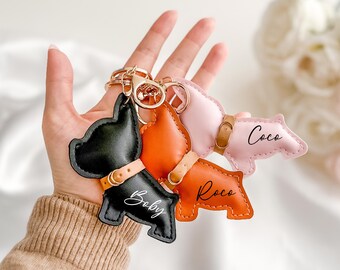 May include: Three leather dog keychain charms in the shape of a French bulldog, with the names "Coco", "Rocco", and "Baby" written on them. The charms are attached to a gold key ring.