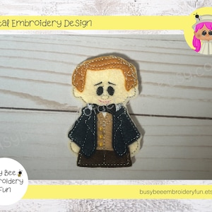 May include: A felt finger puppet of a man with brown hair, wearing a black suit, brown vest, and a bow tie. The puppet is on a white wooden background.