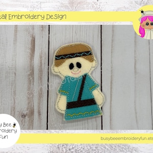 May include: Embroidered felt finger puppet of a boy wearing a blue tunic and brown hat. The puppet is on a white wooden background.