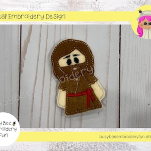 May include: A brown felt finger puppet of a man with a beard and a red sash. The puppet is wearing a brown robe. The image is on a white wood background.