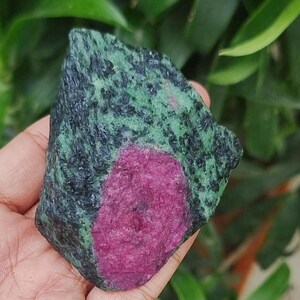 May include: A natural gemstone with a striking magenta ruby set in a dark green and black mineral matrix. The stone has a raw, unpolished look, highlighting its natural beauty. This unique gemstone is ideal for collectors or those interested in jewellery making.