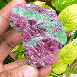 May include: A raw gemstone with a striking colour palette. The stone shows a vibrant mix of deep magenta, light green, and white hues. The surface has a textured appearance, with visible crystalline structures. This natural stone is a unique addition to any collection.