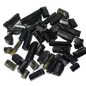 Op de afbeelding: Een verzameling zwarte en groene toermalijnkristallen, ook wel schorl genoemd, in verschillende maten en vormen. De kristallen zijn ruw en onbewerkt, met een natuurlijke, ruwe textuur.
