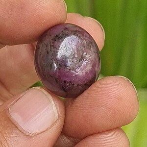 Może przedstawiać: Okrągły, fioletowy kamień szlachetny z ciemnym, prawie czarnym, nakrapianym wzorem. Kamień szlachetny jest gładki i wypolerowany.