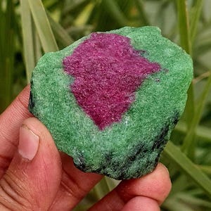 May include: A rough, green and pink gemstone with dark green and black veining. The gemstone is irregularly shaped and has a rough, natural texture.