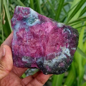 May include: A large, rough, pink and green gemstone with a natural, irregular shape. The gemstone has a mix of pink and green colors with a rough, textured surface.