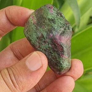 May include: A rough, green and pink gemstone with a mottled surface.