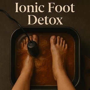 May include: An overhead shot of feet submerged in a dark liquid within a black rectangular basin. A black device with a cord is positioned between the feet. The text "Ionic Foot Detox" is at the top of the image.