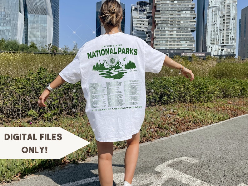 May include: White t-shirt with a green graphic print of mountains and a sun. The text "United States National Parks" is printed above the graphic. The text "The Heart of America's Wildlands" is printed below the graphic.