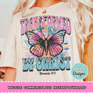 May include: A white t-shirt with a pink and blue graphic design featuring a butterfly and the text "Transformed by Christ" with the scripture reference "Romans 12:2".