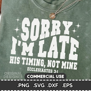 May include: Sage green t-shirt with the text "SORRY I'M LATE" in large white letters. Below, it reads "HIS TIMING, NOT MINE" and "ECCLESIASTES 3:1". A gold necklace with a pendant rests on the shirt. The bottom of the shirt has the words "COMMERCIAL USE".