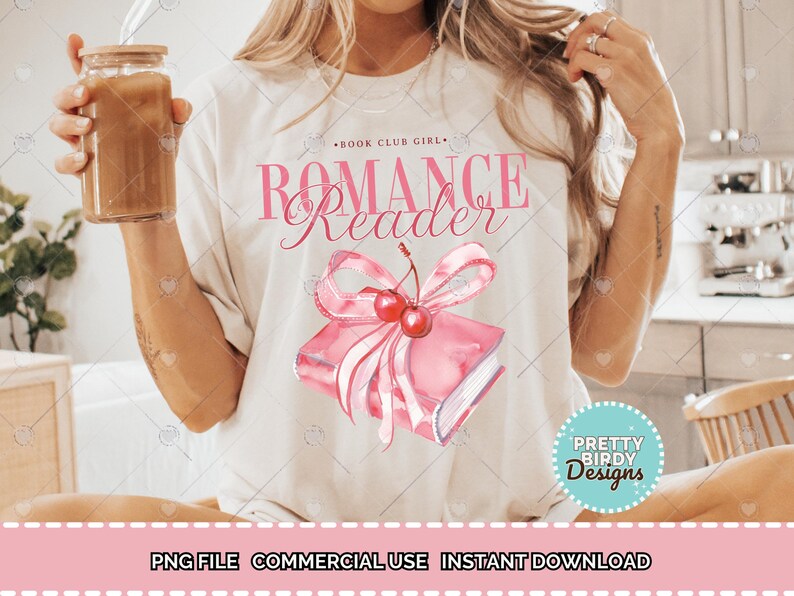以下が含まれることがあります： ピンク色の「ROMANCE Reader」の文字が入ったクリーム色のTシャツ。ピンク色の本にさくらんぼが乗った水彩画イラストが特徴です。Tシャツには、メインテキストの上に「BOOK CLUB GIRL」の文字も入っています。