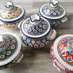 Pode incluir: Um conjunto de cinco tagines de cerâmica coloridos com tampas. As panelas apresentam desenhos intrincados pintados à mão em azul, amarelo, vermelho e verde. Cada panela tem um padrão único e alças brancas.