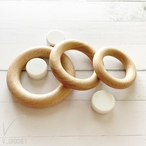 May include: Three wooden rings of different sizes, with a white ring inside each. The rings are stacked on top of each other.