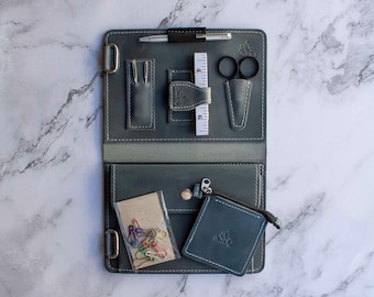 Puede incluir: Un kit de costura de viaje de cuero gris con una bolsa con cremallera, una regla, unas tijeras, un bolígrafo y una variedad de clips de colores.