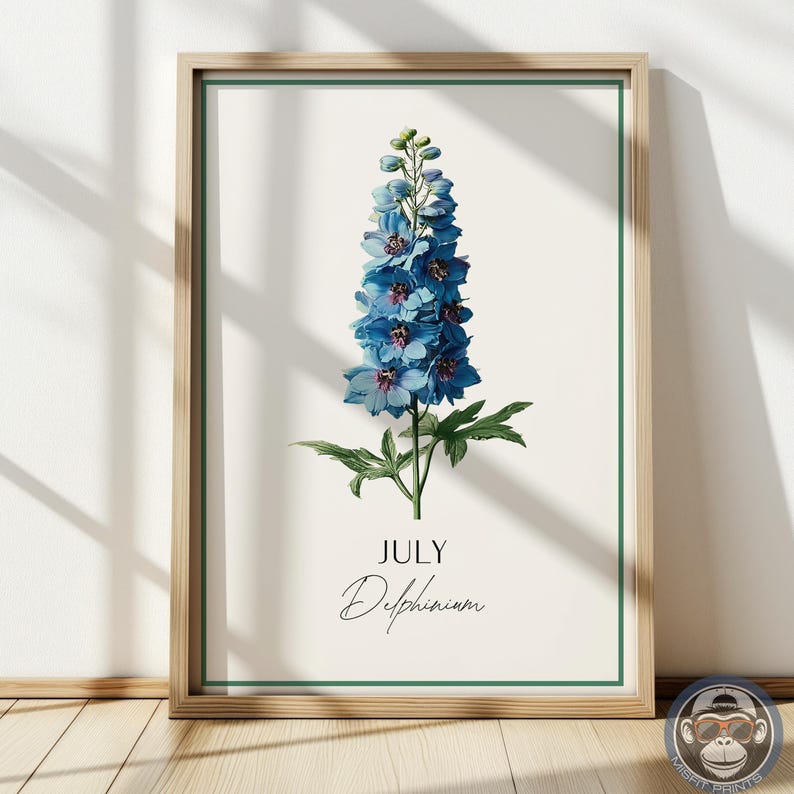 K&ouml;nnte beinhalten: Ein gerahmter botanischer Druck mit einer leuchtend blauen Delphiniumblume. Das Kunstwerk, vor einem cremefarbenen Hintergrund, enth&auml;lt den Text "JULY" und "Delphinium". Der Rahmen ist aus hellem Holz mit einem gr&uuml;nen Rand, geeignet f&uuml;r die Inneneinrichtung.