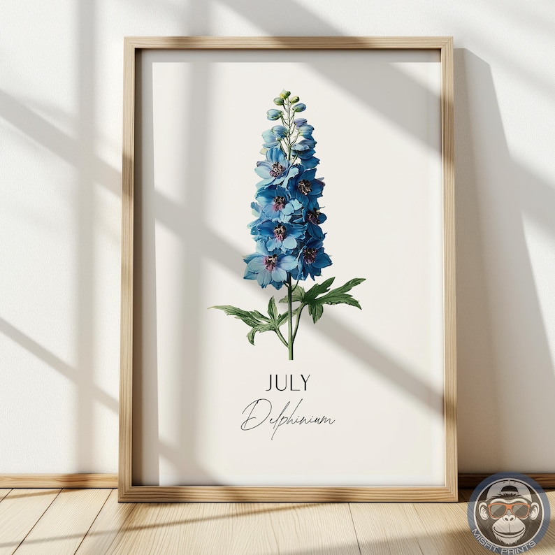 K&ouml;nnte beinhalten: Ein gerahmter botanischer Druck mit einer blauen Delphiniumblume. Das Kunstwerk enth&auml;lt das Wort "JULI" und den Namen der Blume in Schreibschrift. Der Druck ist vor einem cremefarbenen Hintergrund und in hellem Holz gerahmt.
