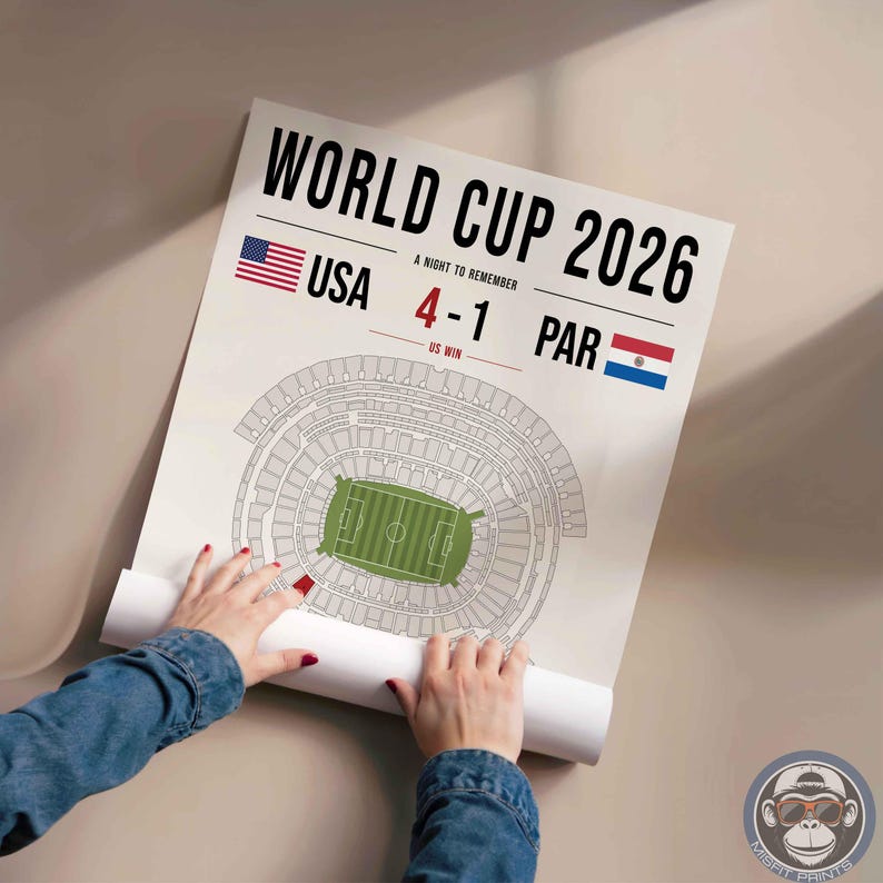 May include: A white poster featuring the text WORLD CUP 2026, A NIGHT TO REMEMBER, and US WIN. It displays the USA and Paraguay flags, the score 4-1, and a top-down architectural diagram of a stadium with a green field in the center.