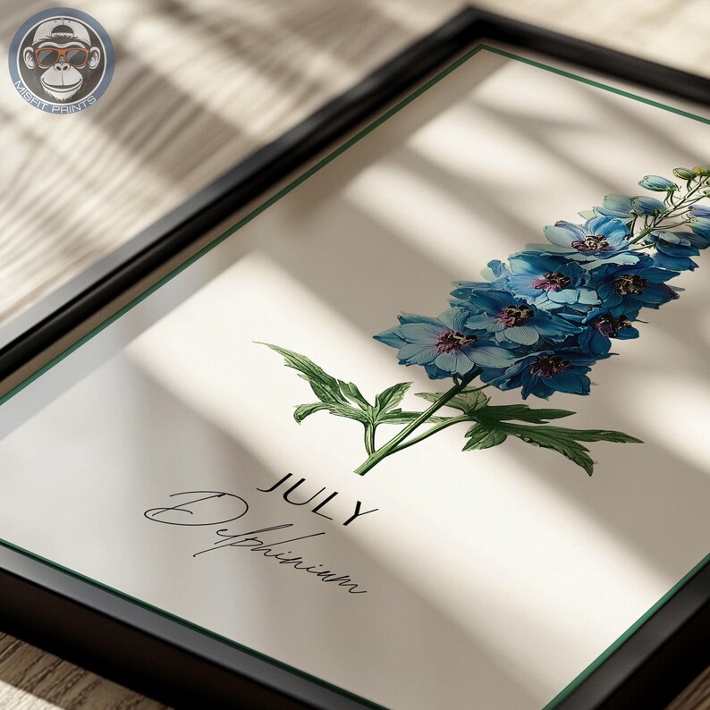 K&ouml;nnte beinhalten: Gerahmter Kunstdruck mit einer detaillierten Illustration einer blauen Delphiniumblume. Das Kunstwerk enth&auml;lt das Wort "JULY" und den Namen der Blume in eleganter Schrift. Der Druck ist in einem schwarzen Rahmen mit wei&szlig;em Rand.