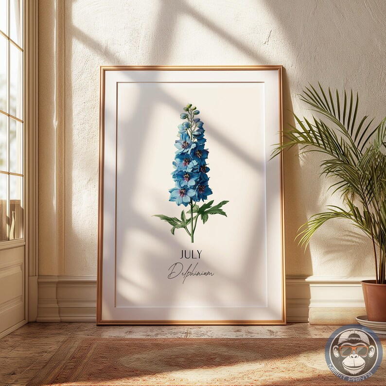 K&ouml;nnte beinhalten: Ein gerahmter botanischer Druck mit einer blauen Delphiniumblume. Der Druck enth&auml;lt das Wort "Juli" und den Namen der Blume, "Delphinium", in Schriftform. Das Kunstwerk ist in einem goldenen Rahmen gefasst und verleiht dem floralen Design einen Hauch von Raffinesse.