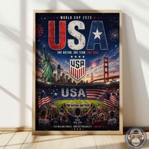 May include: A framed poster for World Cup 2026 featuring the text USA, One Nation. One Team. One Goal. The image displays the Statue of Liberty, the Golden Gate Bridge, a soccer stadium, a USA crest, and a crowd holding a banner with the same text.