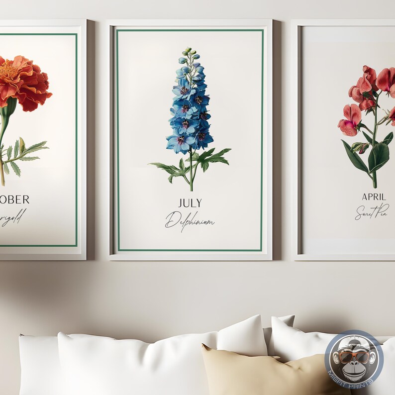K&ouml;nnte beinhalten: Drei gerahmte botanische Kunstdrucke. Der mittlere Druck zeigt eine blaue Delphiniumblume mit dem Text "JULY Delphinium". Die anderen Drucke zeigen eine Ringelblume und eine S&uuml;&szlig;erbse. Jeder Druck hat einen wei&szlig;en Rand und einen gr&uuml;nen Innenrahmen.