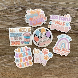 K&ouml;nnte beinhalten: Ein Set mit neun bunten Aufklebern mit Spr&uuml;chen zum Thema Hunde. Die Aufkleber zeigen verschiedene Designs, darunter Pfotenabdr&uuml;cke, Regenb&ouml;gen, Kaffeetassen und Blumen. Der Text auf den Aufklebern enth&auml;lt S&auml;tze wie "Best Dog Mom Ever", "All I Need Is Coffee And My Dog", "Life Is Better With A Dog", "Less People More Dogs", "Fun Mama", "Wife Mother Dog Lover", and "Livin That Dog Mom Life".