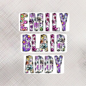 Pode incluir: Tr&ecirc;s adesivos brancos com os nomes "EMILY", "BLAIR" e "ADDY" escritos em letras pretas delineadas. As letras s&atilde;o preenchidas com um padr&atilde;o floral colorido.