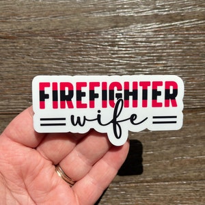 K&ouml;nnte beinhalten: Wei&szlig;er Aufkleber mit dem Text "FIREFIGHTER" in Rot und Schwarz mit einem d&uuml;nnen schwarzen Strich, der die W&ouml;rter trennt. Der Text "wife" ist in schwarzer Kursivschrift mit zwei schwarzen Linien auf jeder Seite des Wortes.