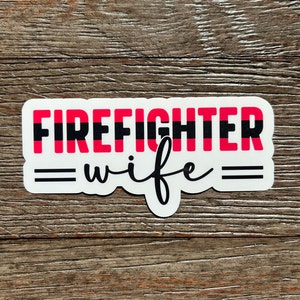 K&ouml;nnte beinhalten: Wei&szlig;er Aufkleber mit schwarzen und roten Streifen und dem Text "FIREFIGHTER" in schwarzen Buchstaben. Unter dem Text befindet sich ein schwarzes Gleichheitszeichen, das Wort "wife" in schwarzer Kursivschrift und ein weiteres schwarzes Gleichheitszeichen.
