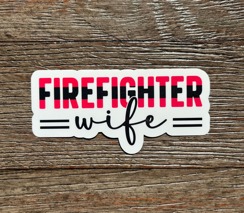 K&ouml;nnte beinhalten: Wei&szlig;er Aufkleber mit schwarzen und roten Streifen und dem Text "FIREFIGHTER" in schwarzen Buchstaben. Unter dem Text befindet sich ein schwarzes Gleichheitszeichen, das Wort "wife" in schwarzer Kursivschrift und ein weiteres schwarzes Gleichheitszeichen.
